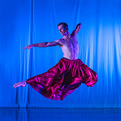 man wearing a red skirt leaps in a dance