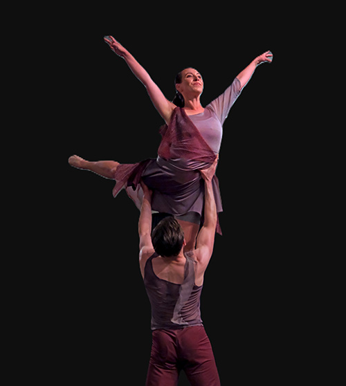 A man lifts up a woman in a dance, both wearing purple