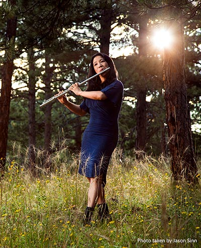 Catherine Peterson playing the flute in a pine forest