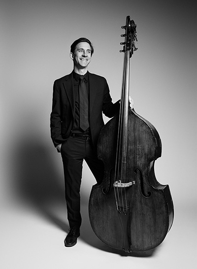 Nicholas Recuber stands smiling with a bass, in black formal wear